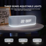 Gray fabric-covered digital alarm clock with an illuminated base on a bedside table, showing “22:00” and temperature, with marketing text about three-level dimmable lighting and a comparison strip labeled 25%, 50%, and 100% brightness.