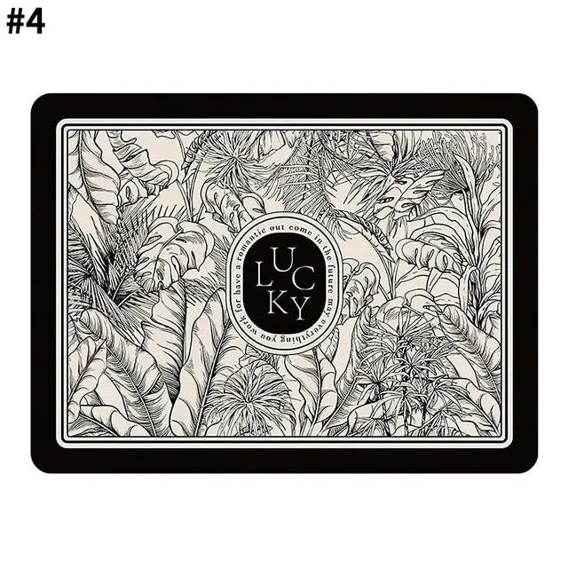 Rectangular decorative mat with a black border, detailed monochrome tropical leaf illustration, and a central circular emblem reading “Lucky,” set against a cream background.