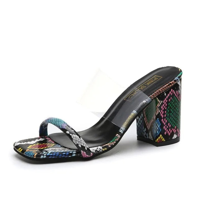 Open-toe mule sandal with a clear upper strap and a multicolor snakeskin-pattern block heel and toe strap, on a black footbed.