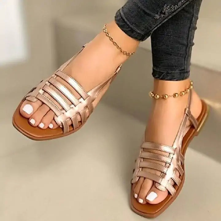 Rose gold flat slingback sandals with multiple metallic straps and square open toes, shown worn with dark skinny jeans.