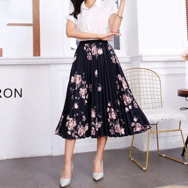 Pleated midi skirt with a gradient design, transitioning from dark black at the waistband to a soft blush pink at the hem, hanging on a black clothing rack next to a vintage-style camera.
