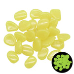 Pile of small, smooth yellow pebble-shaped glow stones on a white background, with a small inset showing them glowing green in the dark.