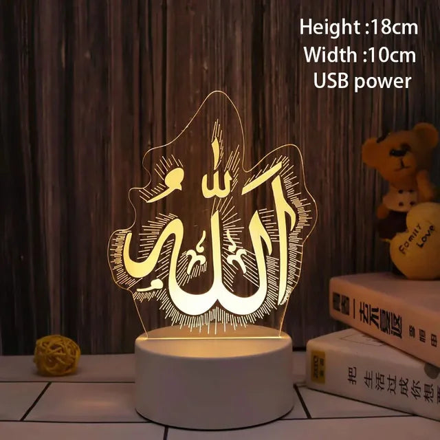 A warm glowing acrylic LED night light featuring Arabic calligraphy for “Allah” on a white round base. The lamp is shown on a tabletop against a wood-panel background, with nearby books and a small teddy bear, and includes text indicating USB power with dimensions of 18 cm height and 10 cm width.