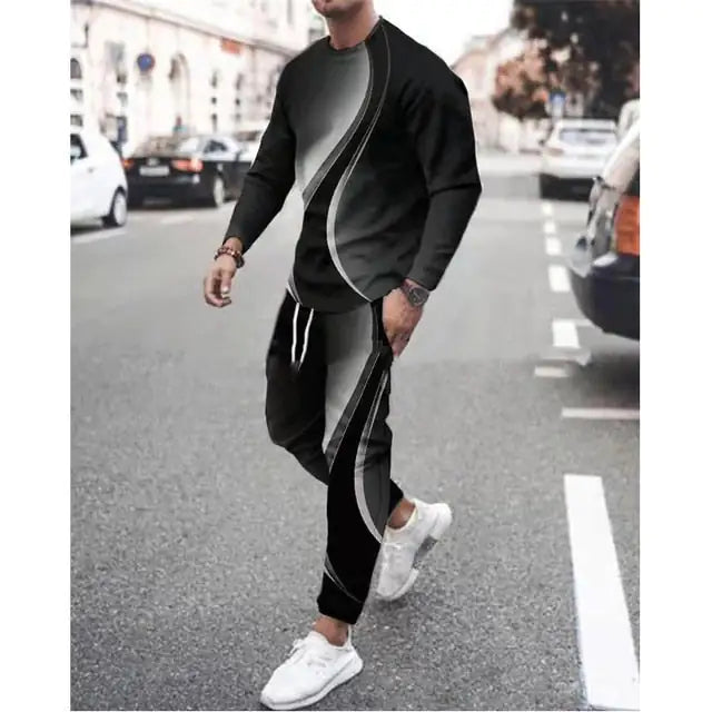 Man walking on a city street wearing a black and gray long-sleeve tracksuit with curved stripe accents, matching jogger pants with a drawstring waist, and white sneakers.
